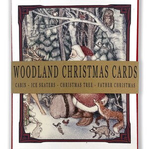 May include: A set of Christmas cards featuring a woodland scene with Santa Claus, a reindeer, a fox, a raccoon, and other animals. The cards are red with a gold border and the text "Woodland Christmas Cards" in gold. The text below the title reads "Cabin - Ice Skaters - Christmas Tree - Father Christmas".