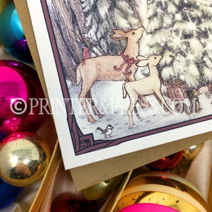 May include: A Christmas card featuring a watercolor illustration of two deer standing in a snowy forest, looking up at a Christmas tree. The deer are brown with red bows around their necks. The card has a brown border and the text "PRINTER & PRESS.COM" is printed in the bottom right corner.