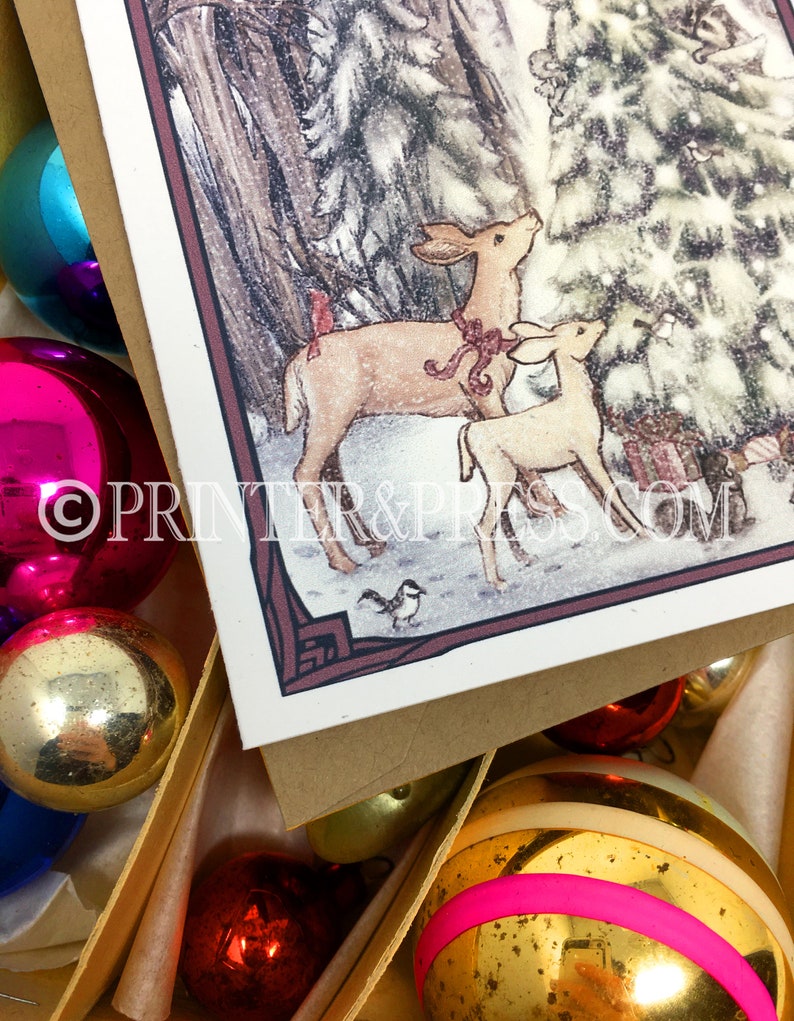 May include: A Christmas card featuring a watercolor illustration of two deer standing in a snowy forest, looking up at a Christmas tree. The deer are brown with red bows around their necks. The card has a brown border and the text "PRINTER & PRESS.COM" is printed in the bottom right corner.