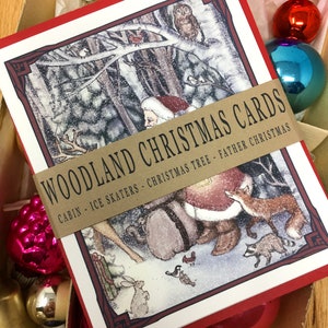 May include: A set of red and white Christmas cards with a woodland scene featuring Santa Claus, a fox, a raccoon, a rabbit, and birds. The cards have a brown ribbon with the text "WOODLAND CHRISTMAS CARDS CABIN - ICE SKATERS - CHRISTMAS TREE - FATHER CHRISTMAS".
