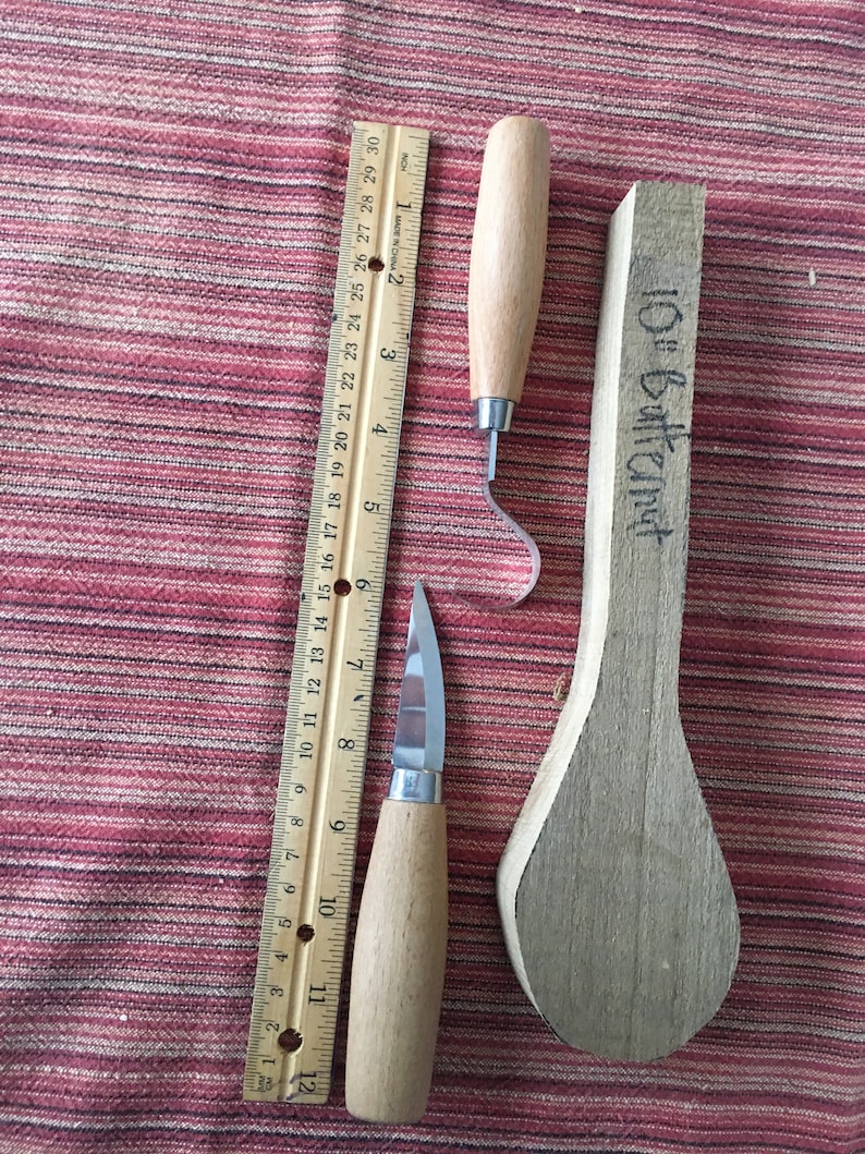 May include: Two wood carving tools with wooden handles and a ruler. The tools are a hook knife and a small knife. The ruler is 12 inches long. The tools are on a red and white striped fabric.
