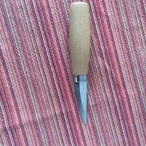 May include: A small, wooden-handled knife with a silver blade. The knife is lying on a striped red and black fabric.