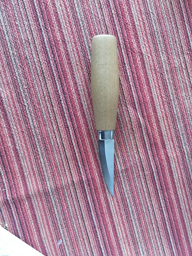 May include: A small, wooden-handled knife with a silver blade. The knife is lying on a striped red and black fabric.