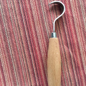 May include: A wooden handled carving tool with a curved metal blade. The tool is on a striped red and white fabric background.