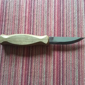 May include: A small, wooden-handled knife with a curved blade. The blade is made of metal and has a sharp point. The handle is made of light brown wood and has a smooth finish.