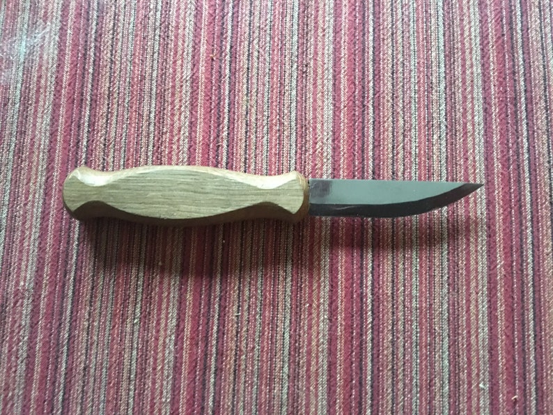 May include: A small, wooden-handled knife with a curved blade. The blade is made of metal and has a sharp point. The handle is made of light brown wood and has a smooth finish.