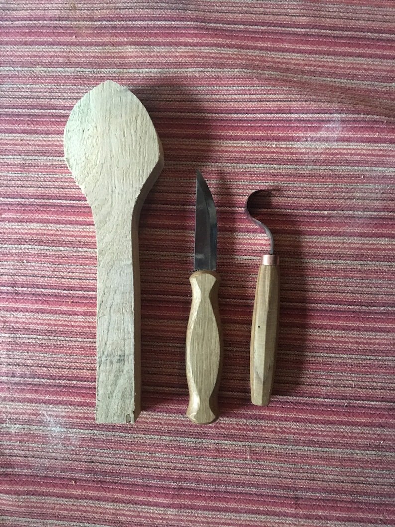 May include: A wooden spoon, a small knife with a wooden handle, and a wood carving tool with a curved blade and wooden handle. The tools are laid out on a red and white striped fabric.