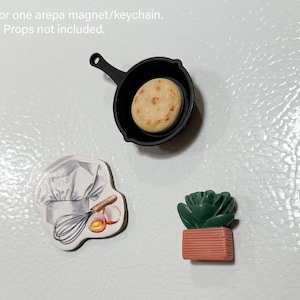 May include: A collection of miniature magnets and keychains. Includes a black skillet with an arepa, a chef's hat with a whisk and eggs, and a green succulent in a terracotta pot. These are perfect for decorating refrigerators or lockers.