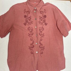 May include: A pink linen button-down shirt with embroidered floral designs on the front.