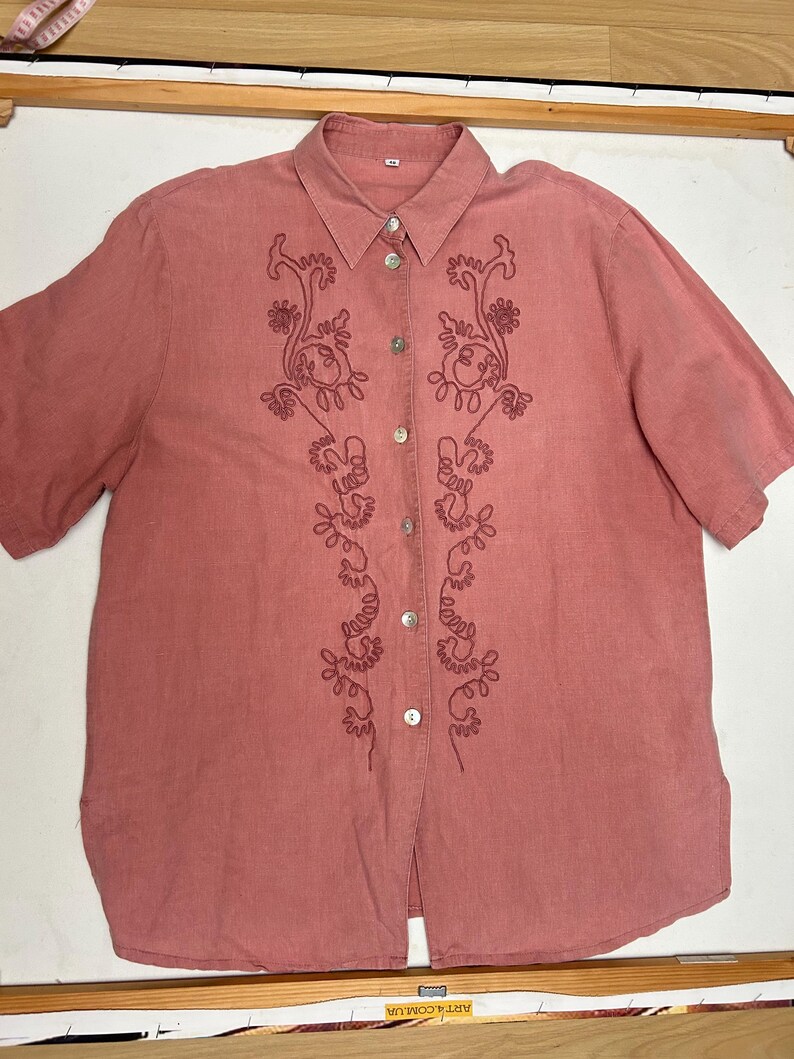May include: A pink linen button-down shirt with embroidered floral designs on the front.