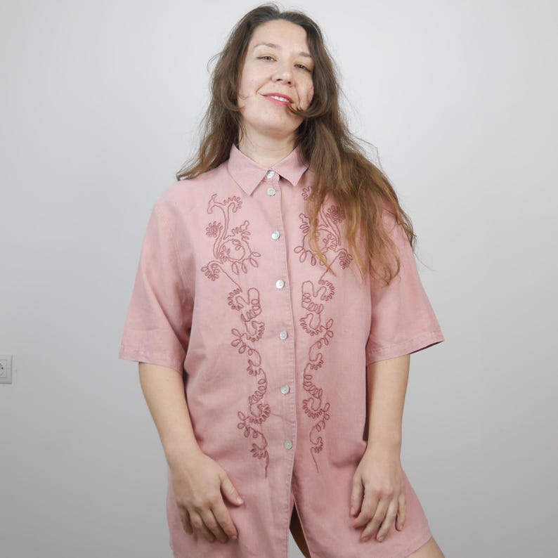 May include: A pink linen shirt with a floral embroidery design. The embroidery is in a darker shade of pink.