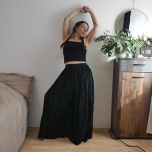 May include: A black crop top and a long, flowing black skirt. The skirt has a wide, gathered waistband and a loose, pleated design. The outfit is simple and elegant, suitable for casual wear or a bohemian style.