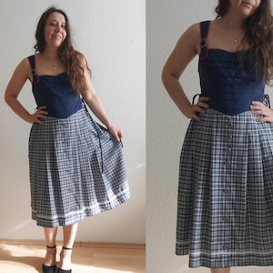 May include: A navy blue and white plaid skirt with a matching navy blue top. The skirt has a button-down front and a pleated design. The top has a square neckline and decorative straps. The outfit is a vintage style.