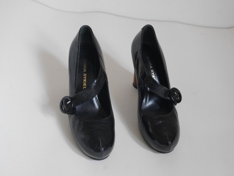 Pode incluir: Par de sapatos de salto alto de verniz preto com uma fivela e o texto "Sonia Rykiel" no interior de cada sapato.