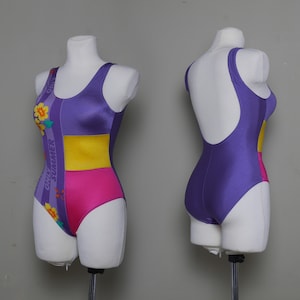 Puede incluir: Un traje de baño morado, rosa y amarillo con estampado floral y el texto "Only Summer" en el lateral.