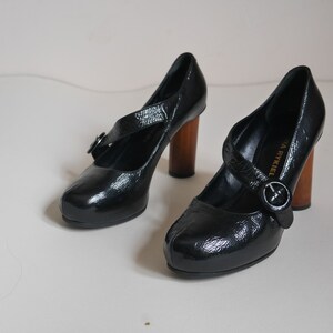 Pode incluir: Um par de sapatos de salto alto de couro preto com uma fivela e saltos de madeira. Os sapatos s&atilde;o da Sonia Rykiel.