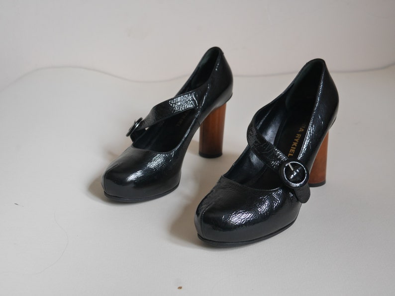 Pode incluir: Um par de sapatos de salto alto de couro preto com uma fivela e saltos de madeira. Os sapatos s&atilde;o da Sonia Rykiel.
