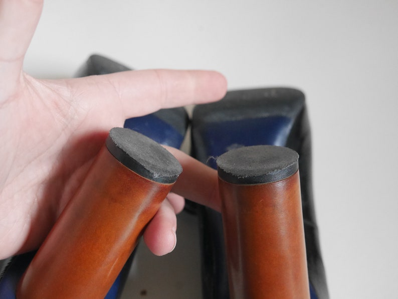 Pode incluir: Close-up da parte inferior de dois sapatos de salto alto. Os saltos s&atilde;o de madeira e t&ecirc;m um acabamento castanho. As solas s&atilde;o de borracha preta.