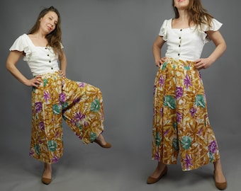 May include: A white blouse with ruffled sleeves and a button-up front paired with wide-leg pants featuring a tropical floral print in shades of brown, green, purple, and white.