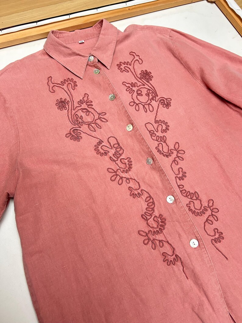 May include: A pink linen button-down shirt with a floral embroidery design.