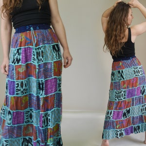 Op de afbeelding: Een lange, zwierige patchwork rok met een strikband. De rok is gemaakt van verschillende stoffen in tinten blauw, paars, oranje en zwart. De rok is een goede keuze voor een bohemian of hippie stijl.