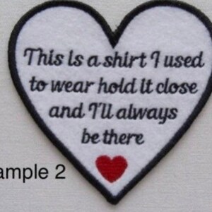 May include: A heart-shaped patch with a white center and black border. The patch features the text "This is a shirt I used to wear hold it close and I'll always be there." A small red heart is at the bottom.