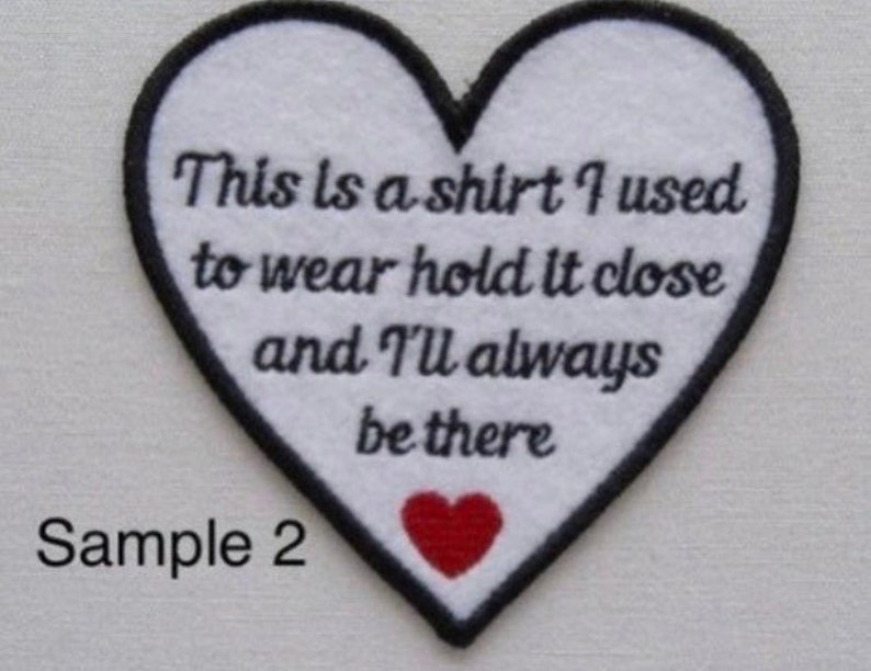 May include: A heart-shaped patch with a white center and black border. The patch features the text "This is a shirt I used to wear hold it close and I'll always be there." A small red heart is at the bottom.