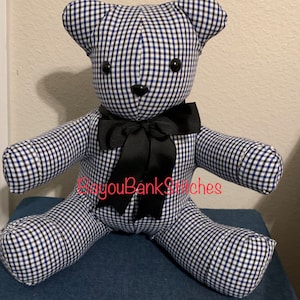 May include: A handmade teddy bear with a blue and white gingham pattern. The bear has black button eyes, a black nose, and a black ribbon bow. The text "BayouBankStitches" is written across the bear.