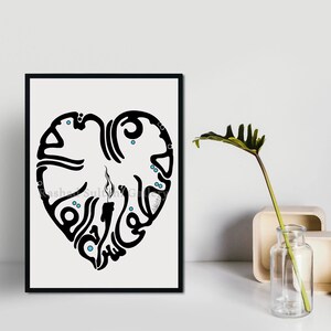 May include: Black and white calligraphy art print of a heart with the word "love" written in Arabic script. The print is framed in a black frame and is hanging on a white wall.