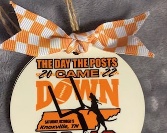 May include: A round white ornament featuring an orange and white checkered bow and twine hanger. The graphic displays the text THE DAY THE POSTS CAME DOWN 2022, a football goalpost, a silhouette of a dog, the state of Tennessee, and 52 49.