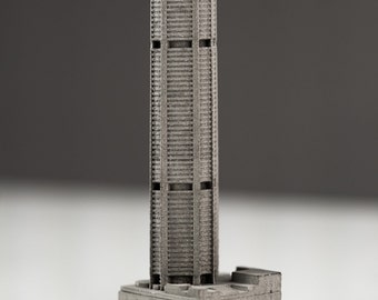 May include: A miniature model of a skyscraper made of gray metal. The model is detailed with windows and a base.