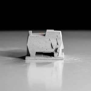 May include: A small, grey concrete sculpture of a building with geometric shapes and a flat base.