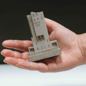 May include: A small, grey concrete model of a building with the text "DORMAN LONG" on the front.