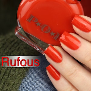 Puede incluir: Un frasco de esmalte de uñas rojo brillante con la palabra "Rufous" en fuente roja y blanca. Las uñas están pintadas del mismo color rojo vibrante. La botella tiene las letras "P O H".