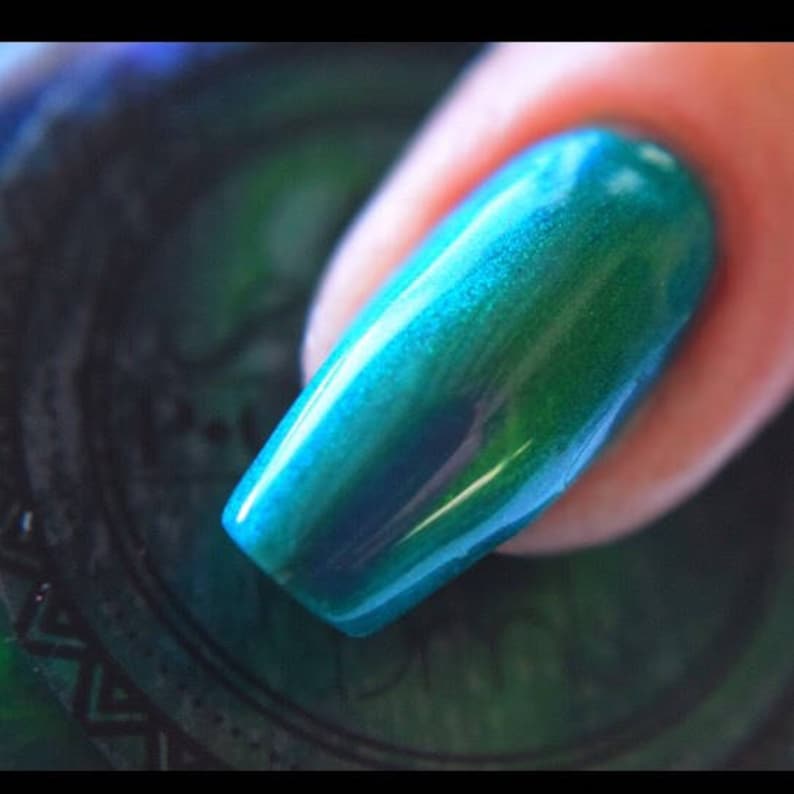 K&ouml;nnte beinhalten: Nahaufnahme eines Fingernagels, der mit schimmerndem t&uuml;rkisfarbenem Nagellack lackiert ist. Der Lack hat ein gl&auml;nzendes Finish und reflektiert das Licht, wobei Blau- und Gr&uuml;nt&ouml;ne zu sehen sind. Der Nagel ist lang und oval geformt.