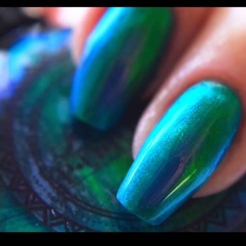 K&ouml;nnte beinhalten: Nahaufnahme von lackierten Fingern&auml;geln mit schimmerndem, irisierendem Effekt. Die N&auml;gel gehen von einem tiefen Teal zu einem leuchtenden T&uuml;rkis &uuml;ber und erzeugen einen mehrdimensionalen, auff&auml;lligen Look. Der Lack hat ein gl&auml;nzendes Finish.