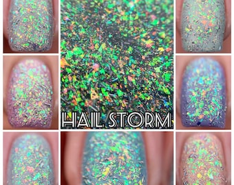May include: Close-up of several manicured nails showcasing a nail polish called "Hail Storm." The polish features a base color with iridescent, colorful flakes. The colors include green, orange, and silver.