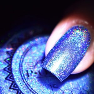 May include: Close-up of a fingernail painted with iridescent blue nail polish. The polish has a shimmering, holographic effect, reflecting multiple colors. The image is set against a dark background, highlighting the vibrant nail color.