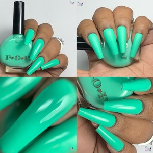 May include: A bottle of teal nail polish with a black cap next to long, teal-colored acrylic nails. The nail polish bottle has the word "POP" printed on it. The nails are a solid, matte color.