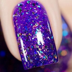 May include: Close-up of a fingernail with vibrant purple nail polish. The polish is heavily embellished with iridescent, multi-colored glitter flakes, creating a sparkling, textured effect. The nail is rounded and polished.