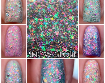 May include: Close-up of several manicured nails showcasing a nail polish with a holographic, iridescent effect. The polish has a glittery, multi-colored appearance. The image also features the text "SNOW GLOBE".