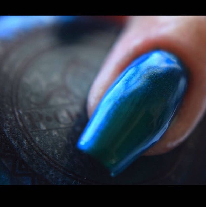 K&ouml;nnte beinhalten: Nahaufnahme eines Fingernagels mit einer langen, ovalen Form. Der Nagel ist mit einem gl&auml;nzenden, irisierenden Lack lackiert, der zwischen Blau- und Gr&uuml;nt&ouml;nen changiert. Der Nagel ist gut manik&uuml;rt und reflektiert das Licht.