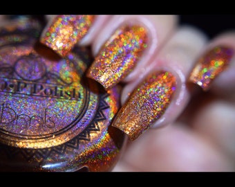 May include: Close-up of a bottle of nail polish and manicured nails. The nails are covered in a sparkly, iridescent orange and gold polish. The bottle is brown with a decorative label. The nail polish is labeled "DP Polish".