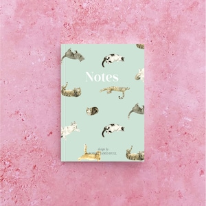 Puede incluir: Un cuaderno azul claro con un patrón repetitivo de gatos en varias poses. La portada dice "Notes" y "design by ROBERT JAMES HULL".