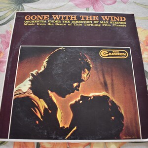 May include: A vintage vinyl record album cover featuring a black and white silhouette of a couple embracing. The album cover is titled "Gone With The Wind" with the text "Orchestra Under The Direction Of Max Steiner" and "Music from the Score of This Thrilling Film Classic". The album cover also features the RCA Camden logo.