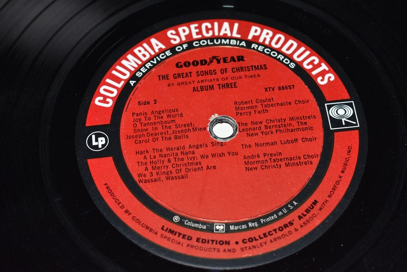 May include: A red vinyl record with the text "Columbia Special Products" and "Goodyear The Great Songs of Christmas" on a black background. The record is labeled "Side 2" and lists the songs and artists on the record. The record is part of a limited edition collectors' album.