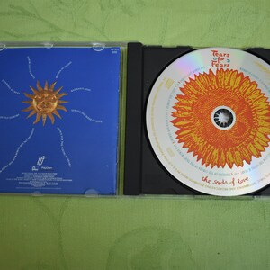 May include: A CD case with a blue background and a sun with a face in the center. The CD is in a black case with a yellow sunflower design and the text "Tears for Fears The Seeds of Love".