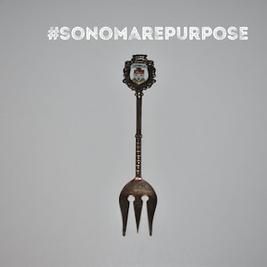 May include: Silver souvenir fork with a decorative handle featuring a crest with a red and white design. The handle is engraved with the text "#SONOMAREPURPOSE".