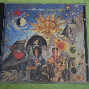 May include: A CD case with a colorful, surreal artwork featuring two figures, a sun, and a heart. The text on the case reads "Tears for Fears The Seeds of Love".