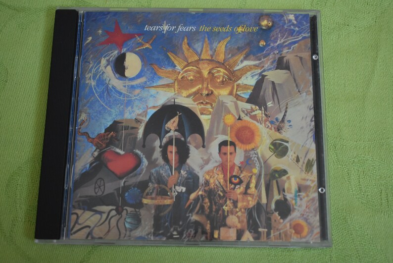May include: A CD case with a colorful, surreal artwork featuring two figures, a sun, and a heart. The text on the case reads "Tears for Fears The Seeds of Love".